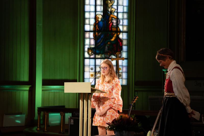 Serine Masterbakk-01661.jpg Ei kvinne talar i ei kyrkje. Ei eldre kvinne står att med ho.